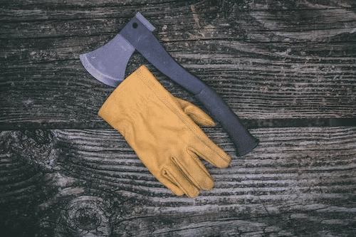 An exciting scene from an axe throwing game - A pair of gloves resting beside a sturdy axe on the floor, ready for players to engage in the thrilling challenge of axe throwing.