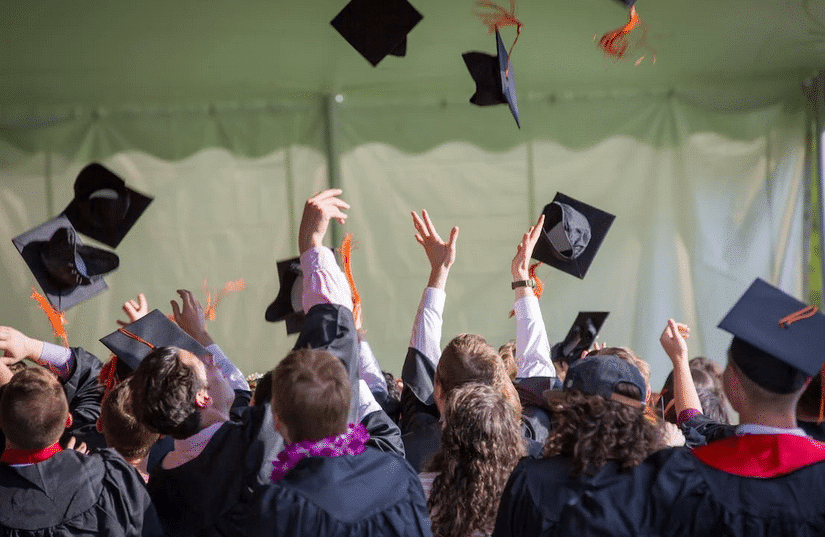 Excited students celebrating graduation by throwing their caps into the air at an 'Axe Throwing Party' filled with joy and triumph.